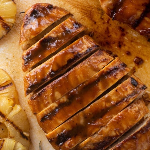 Top down shot of sliced grilled pineapple chicken breast on a white cutting board with rings of grilled pineapple next to it.