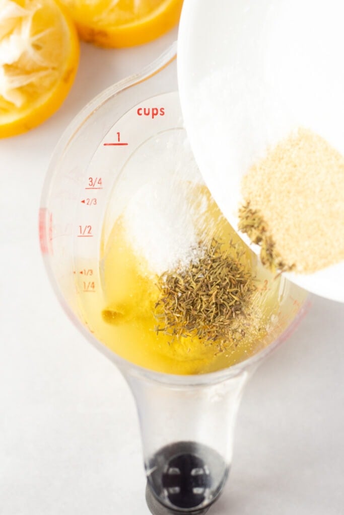 Pouring spices into a measuring cup that's filled with oil and lemon juice.
