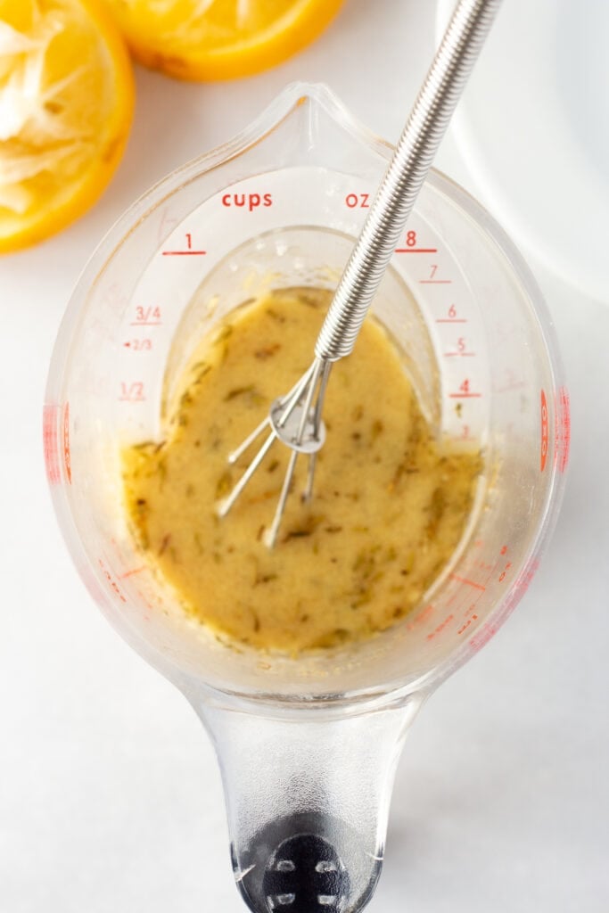 Top down shot of a plastic measuring cup with a small whisk in it and a dijon thyme marinade.