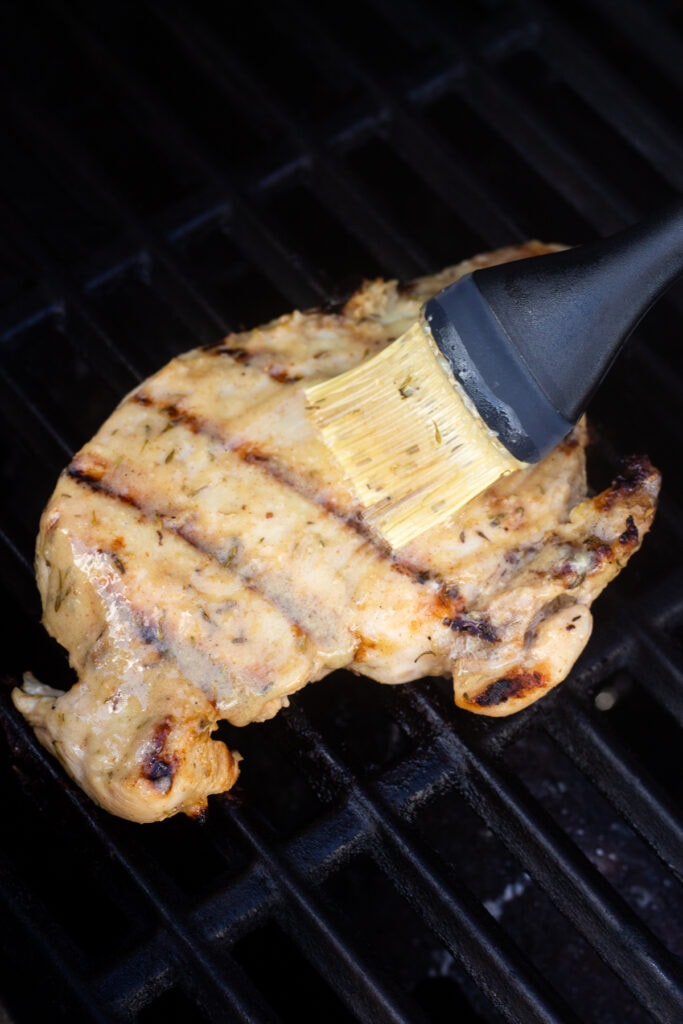 A basting brush putting a glaze on top of grilled chicken while it's grilling.