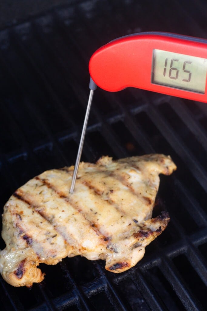 A red meat thermometer taking the temperature of a grilled chicken breast. The temp reads 165F.