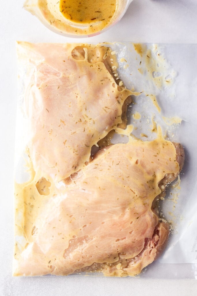 Top down shot of raw chicken breasts marinating in a ziploc bag.