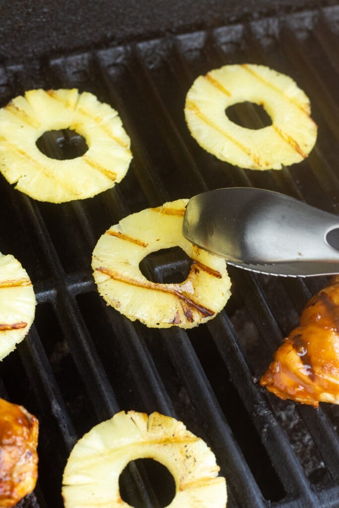 A pair of tongs flipping canned pineapple slices over on a grill.