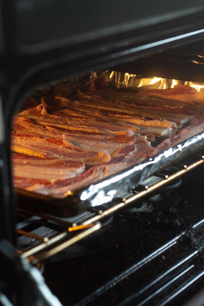 Raw bacon on a foil-lined baking sheet going into a cold oven.