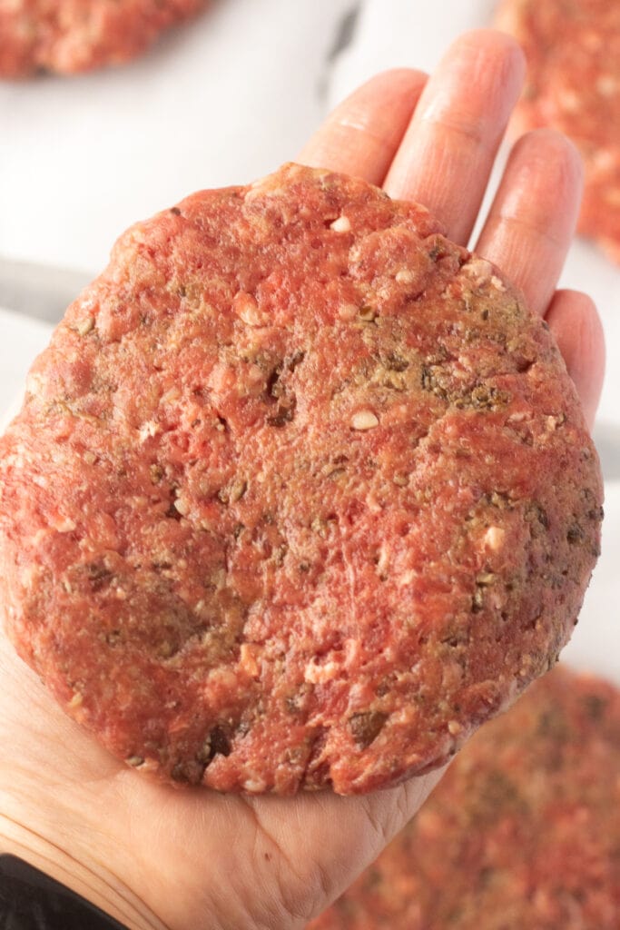 Close up of a hand holding a circular raw burger patty in it.