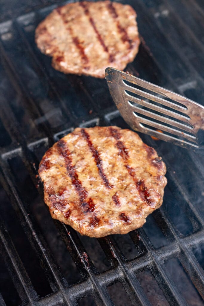 A grilled hamburger patty that's been flipped over by a metal spatula on a grill.