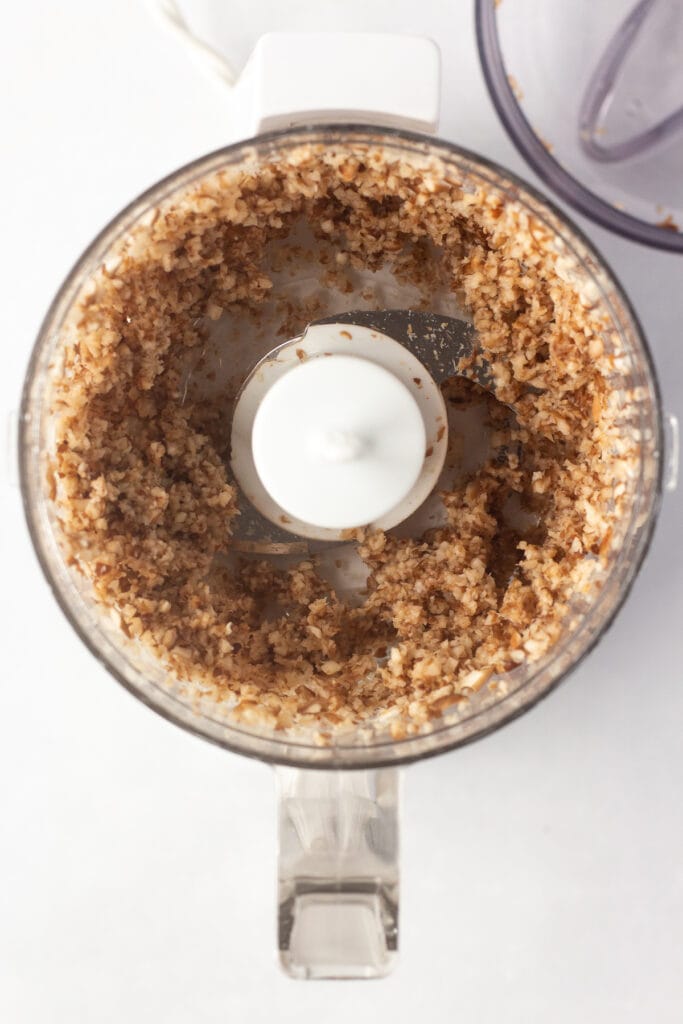 Top down shot of minced shiitake mushrooms in a small food processor on a white background.