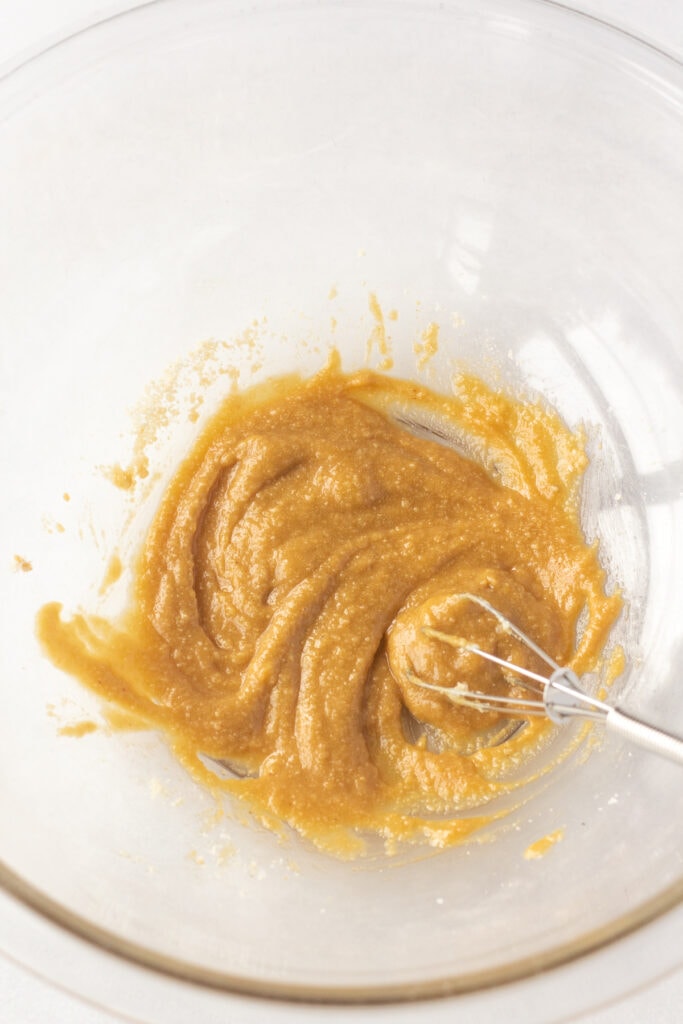 Close up of seasonings and almond flour being mixed in a clear bowl with a small whisk.