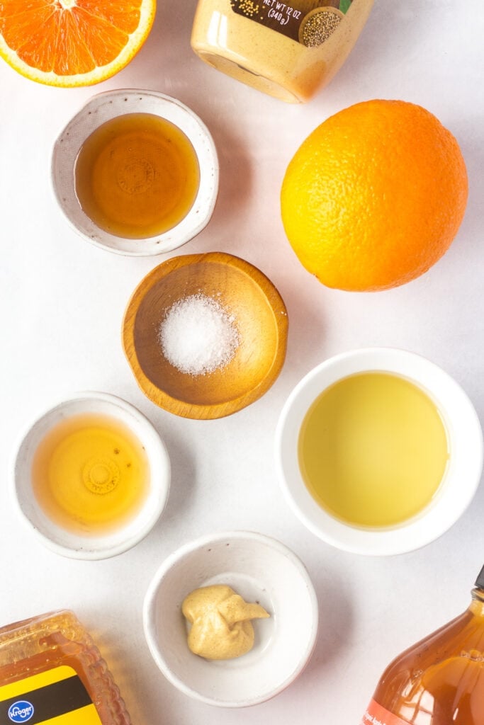 Top down shot of ingredients for honey orange vinaigrette in small white bowls on a white background.