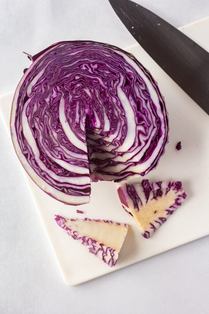 Half a purple cabbage on a white cutting board with the inner stem cut out of it.