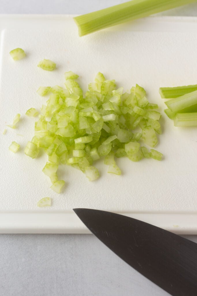 Diced celery on a white cutting board with a large knife.