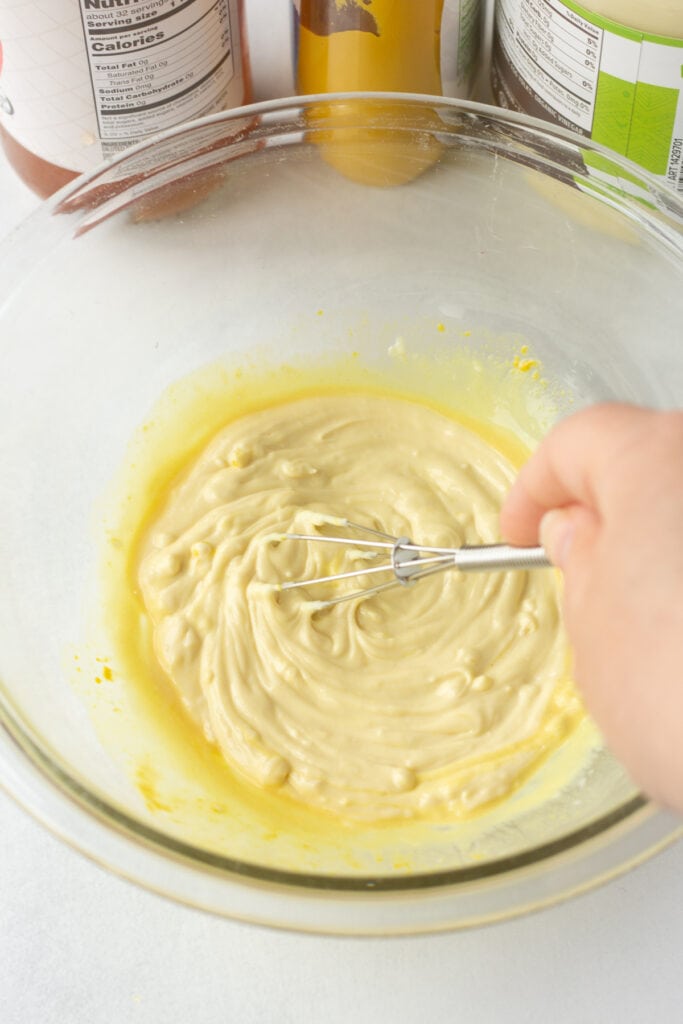Close up of mayo, mustard, and apple cider vinegar being mixed with a small whisk in a small bowl.