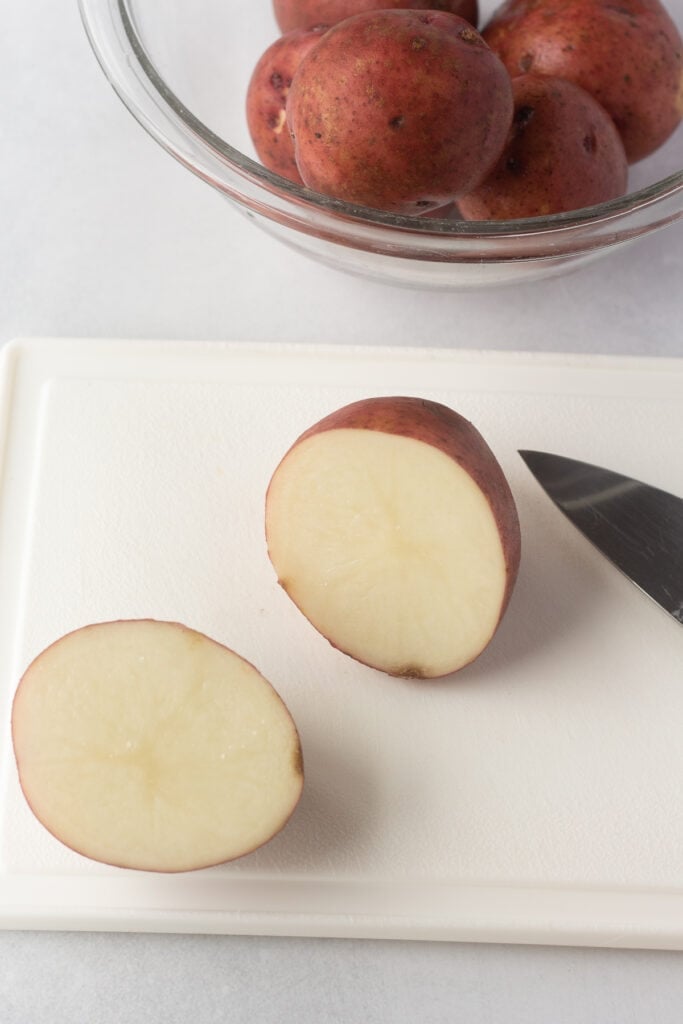 Cutting raw red potatoes on a white cutting board with a large knife.