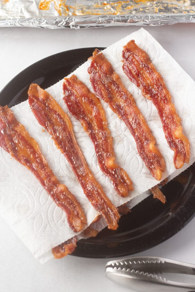 Cooked strips of bacon resting on a black plate lined with paper towels.
