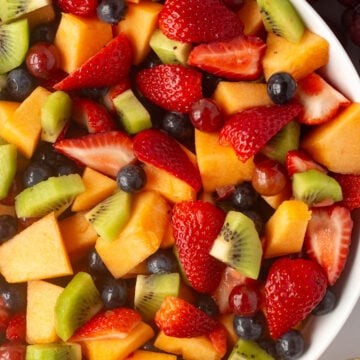 Top down shot of a white bowl with mixed fruit salad in it, surrounded by fresh fruit on the sides.