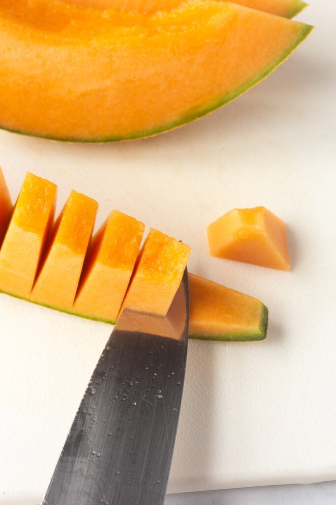 Cutting off small sectioned off pieces of cantaloupe from the rind.