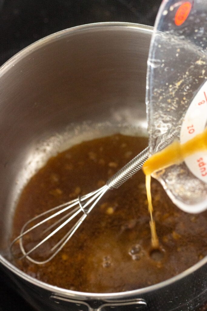 Pouring a brown marinade into a small saucepan with a whisk in it.