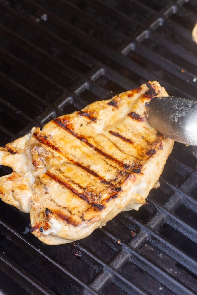 Metal tongs flipping a chicken breast over on a grill.