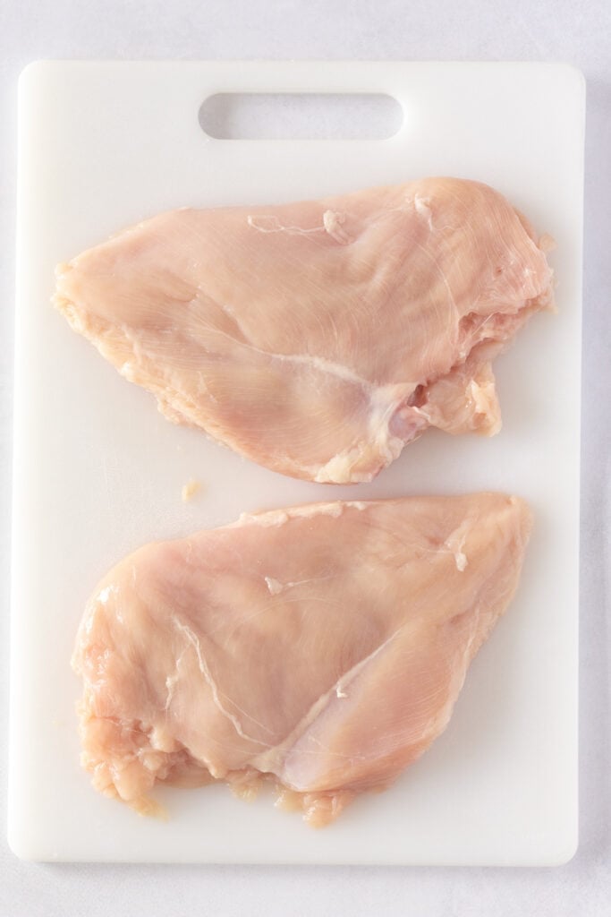 Two flattened chicken breasts on a white cutting board.