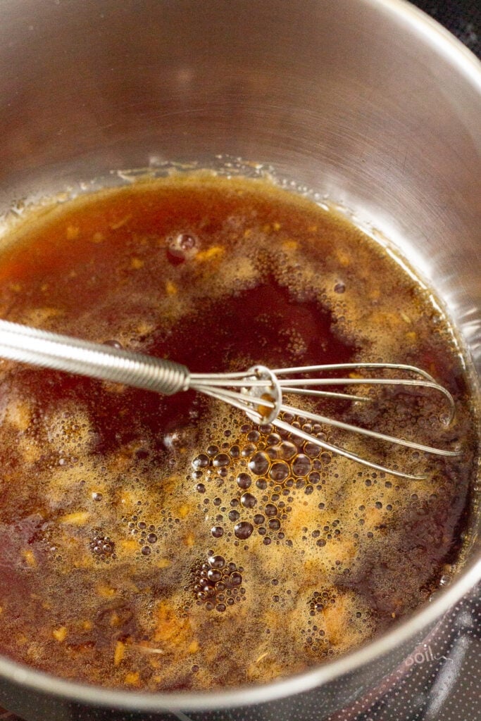 Close up of a soy honey brown marinade in a small saucepan being boiled with a whisk in it.