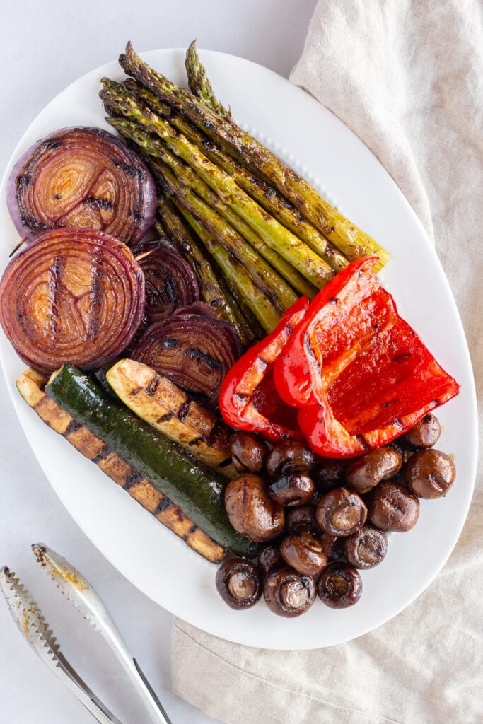 Top down shot of a white oval platter with marinated grilled veggies on them.