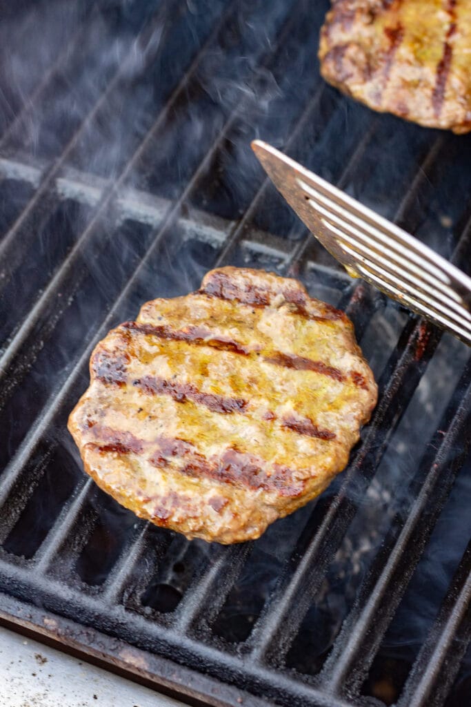 A silver metal spatula flipping over a curry burger on a hot grill.