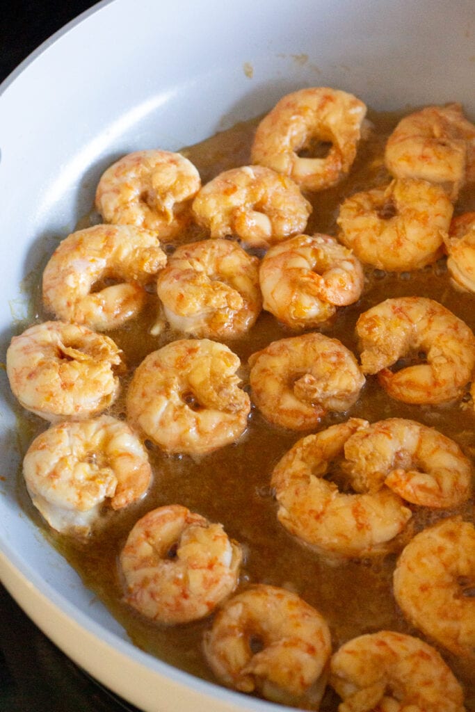 Orange shrimp cooking in a pan on the stove top.