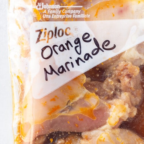Raw chicken thighs in a ziploc bag in an orange juice marinade.