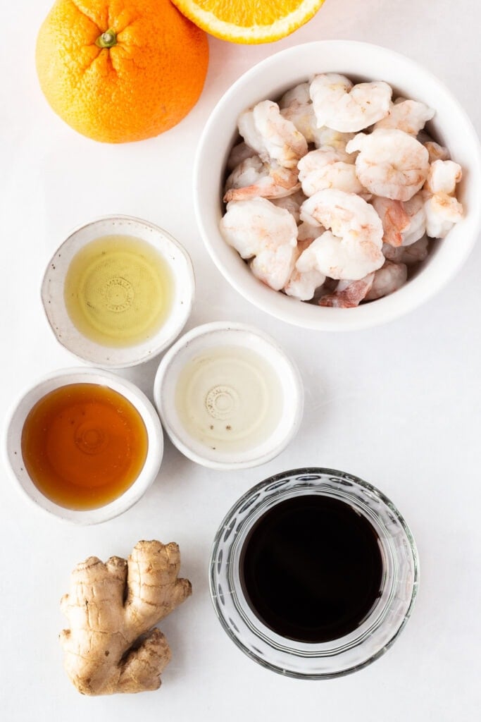 Top down shot of ingredients for shrimp marinated in orange juice, including soy sauce, honey, rice vinegar, ginger, and oil.