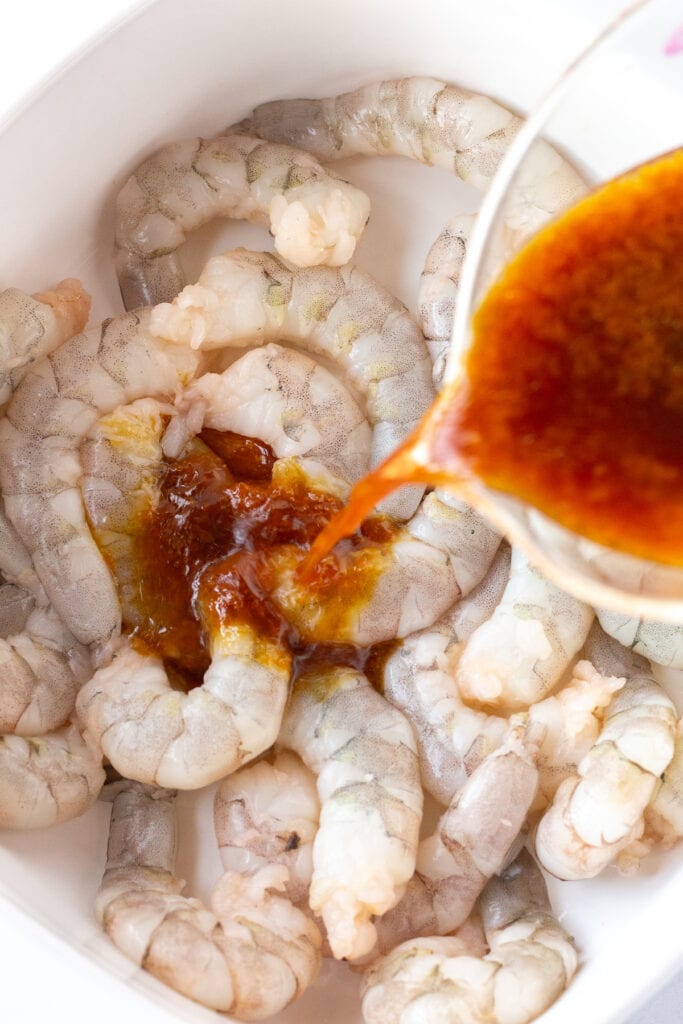 Pouring orange juice marinade over raw shrimp in a white square dish.