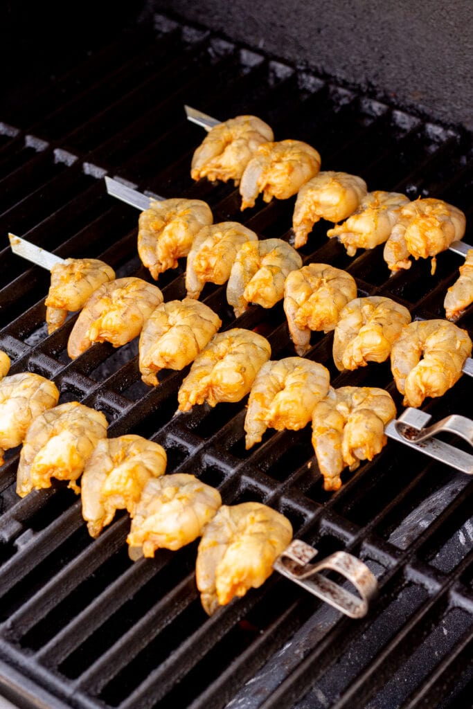 Raw marinated shrimp on metal skewers on a hot grill.