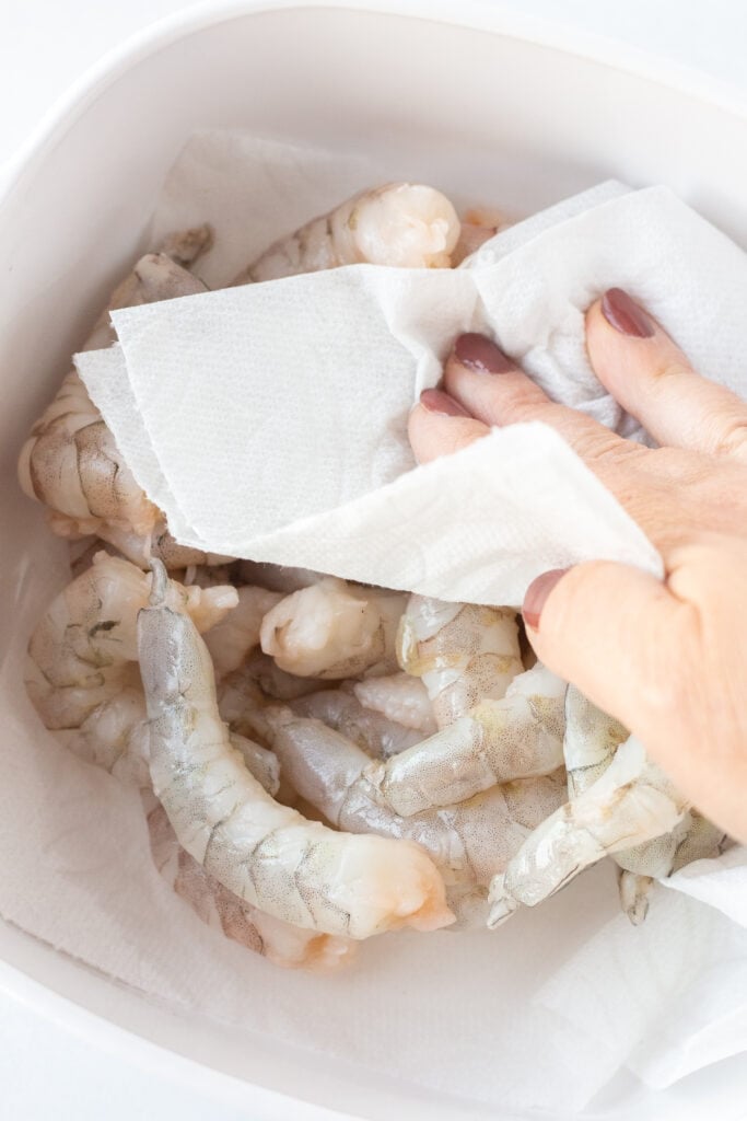 A hand blotting at raw shrimp with a paper towel.