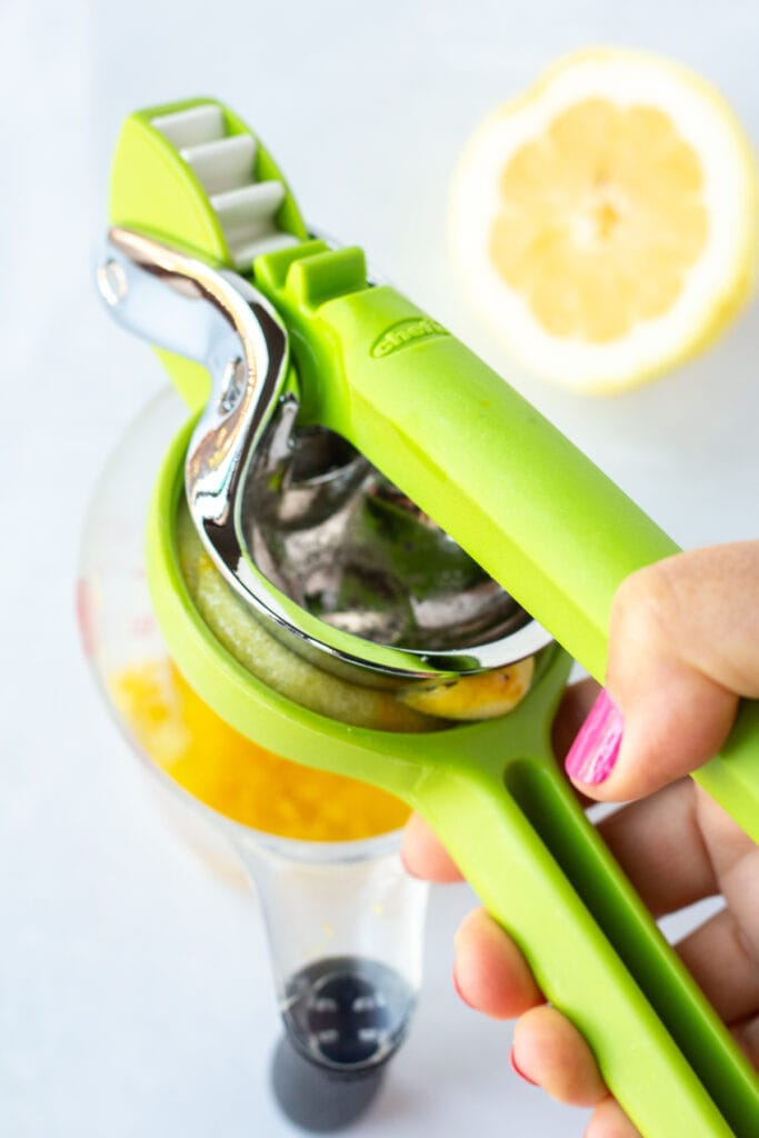 A hand juicing a lemon with a handheld juicer that's green.