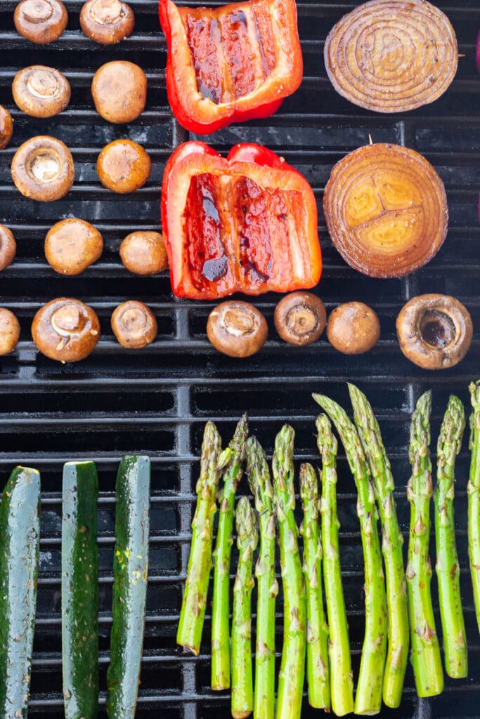 Mushrooms, bell peppers, onion, zucchini, and asparagus cooking on a hot grill.