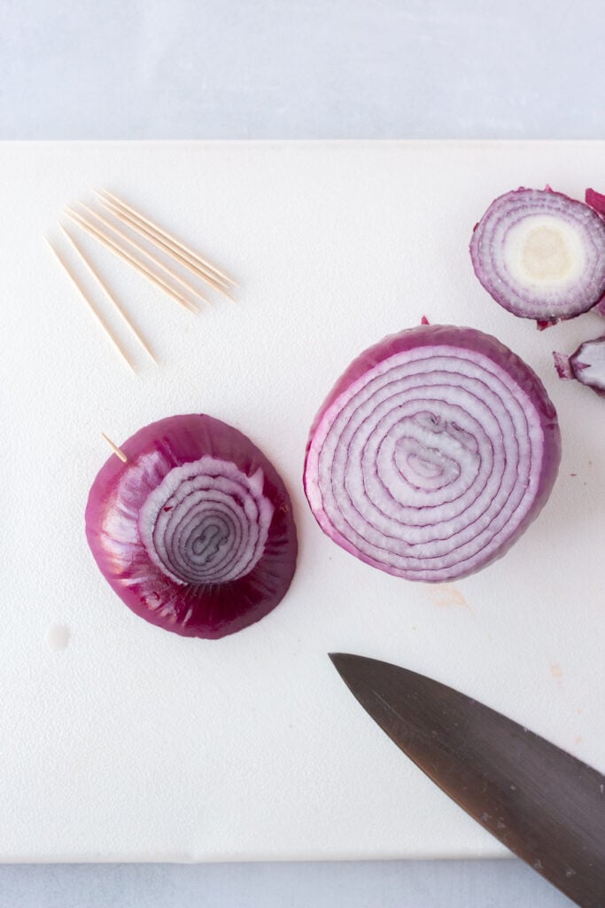 Slicing a red onion into half inch thick slices on a white cutting board.