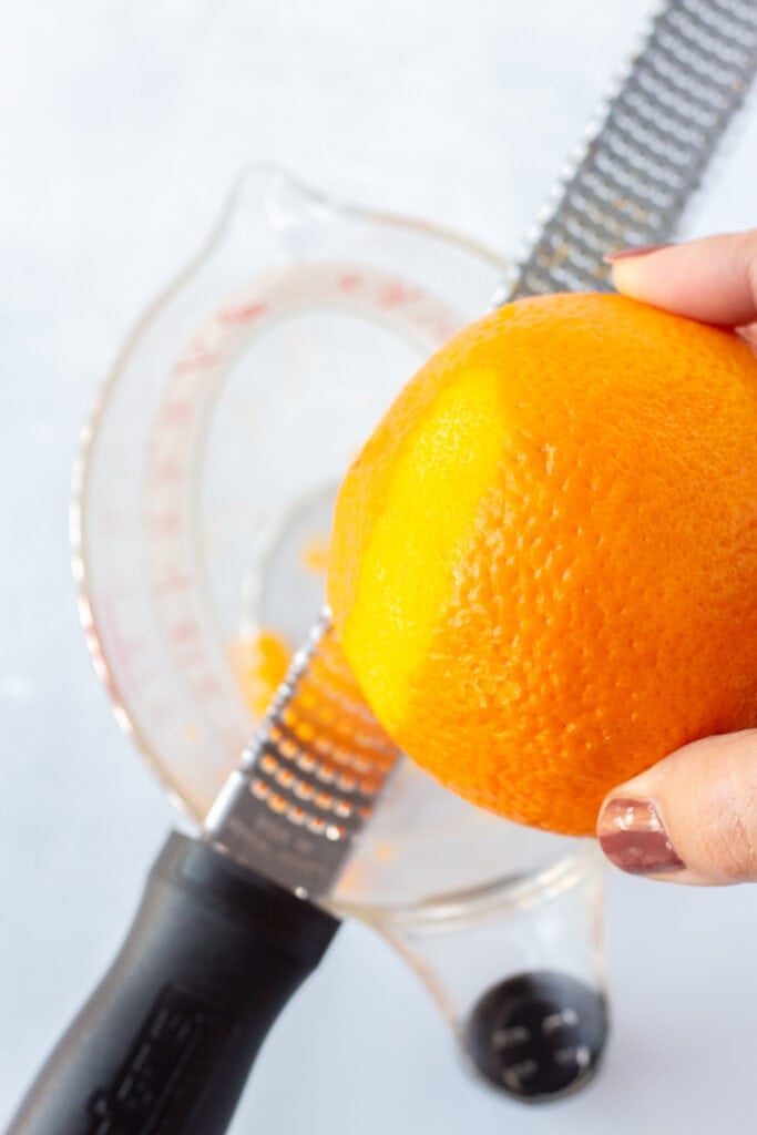 Zesting an orange with a microplane over a liquid measuring cup.