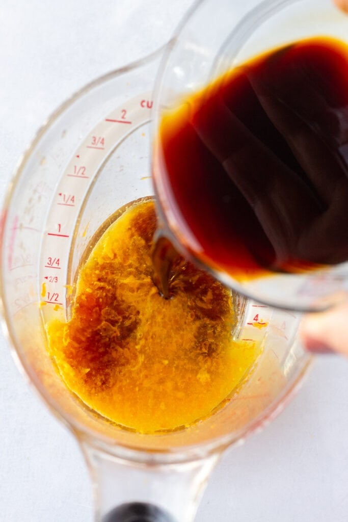 Pouring soy sauce into a measuring cup with orange juice and zest in it.