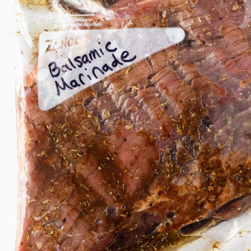 A flank steak in a plastic ziploc bag with a balsamic marinade in it, and the words "balsamic marinade" written in black market on the bag.
