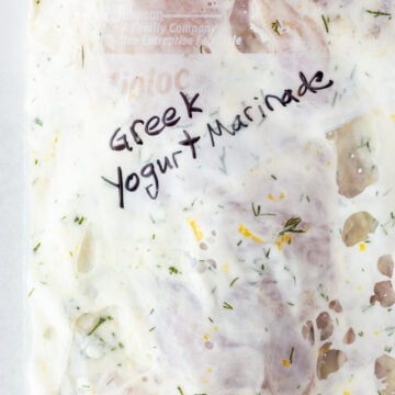 Close up of some chicken thighs covered in a white marinade in a ziploc bag that reads "Greek Yogurt Marinade"