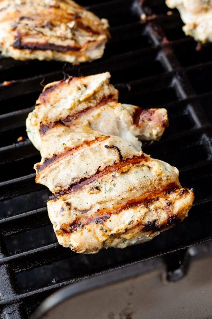 A greek marinated boneless chicken thigh being cooked on a grill.