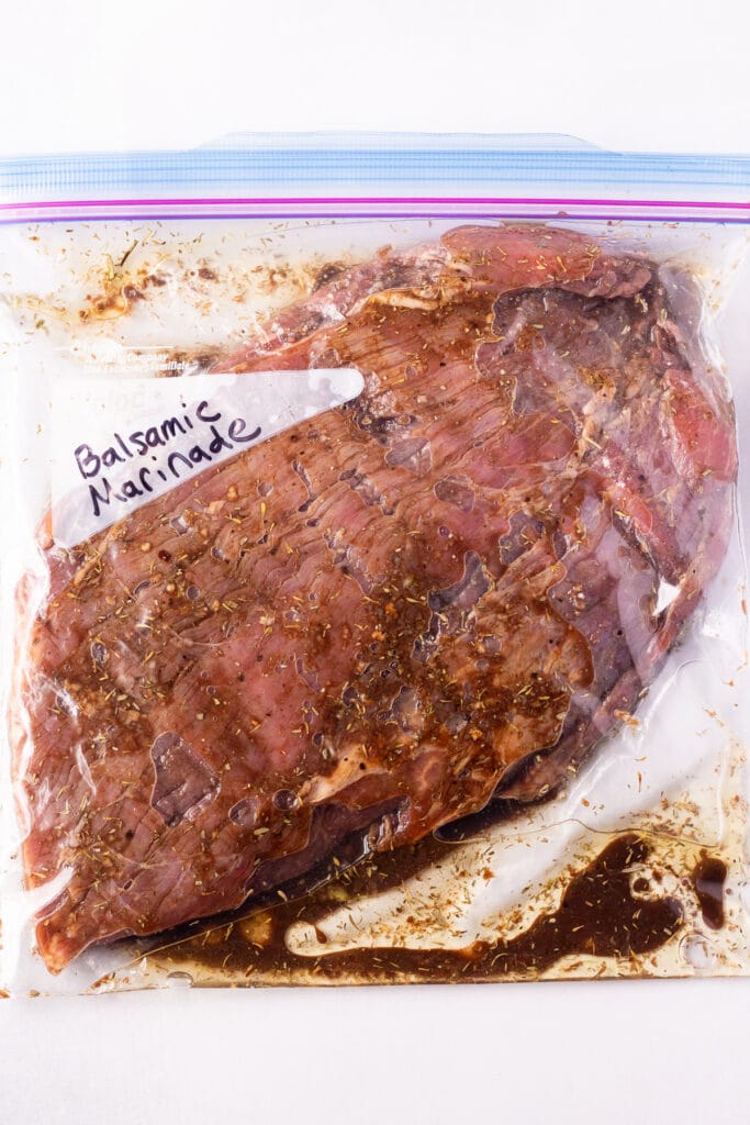 Top down shot of a ziploc plastic bag with raw steak marinating in a balsamic marinade in it.