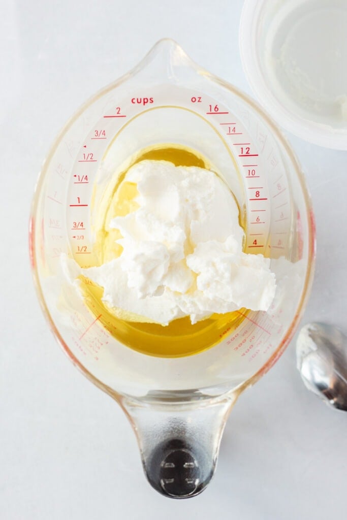 Top down shot of oil and plain Greek yogurt in a measuring cup on a white background.