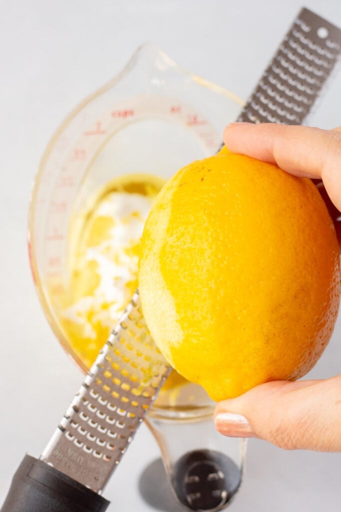 Zesting a lemon over a measuring cup with oil and yogurt already in it.