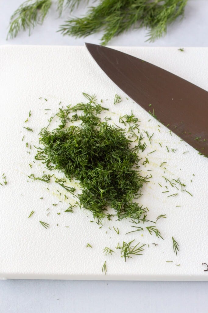 Finely chopped fresh dill fronds on a white cutting board with a knife next to them.