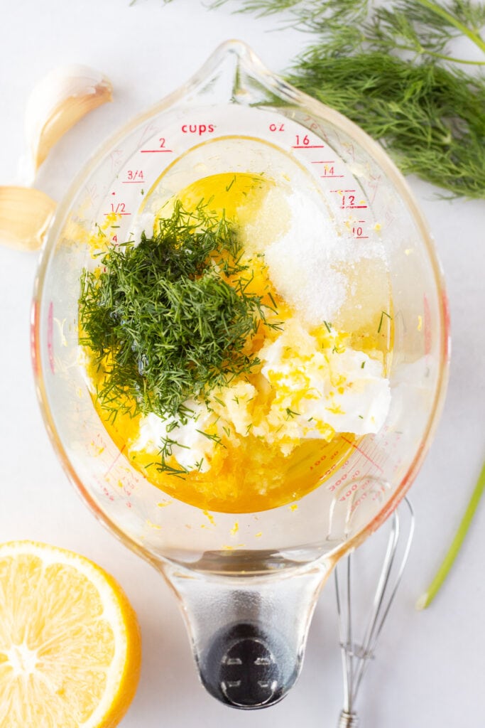 Ingredients for a Greek yogurt marinade, including fresh dill, garlic, lemon juice and zest, and kosher salt, in a measuring cup.