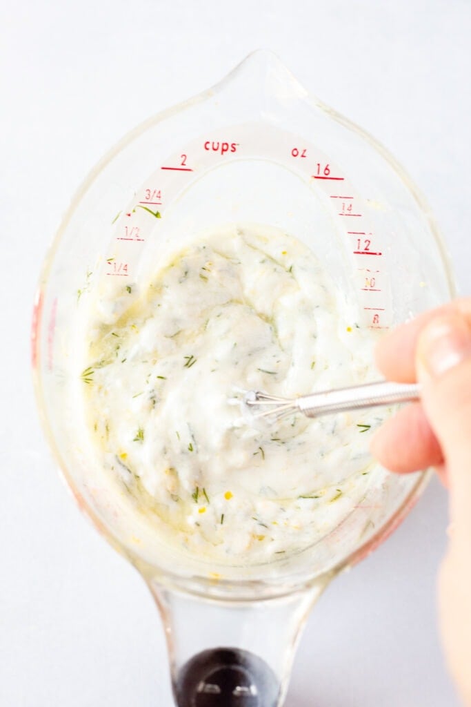 Whisking together ingredients for Greek yogurt marinade in a measuring cup.