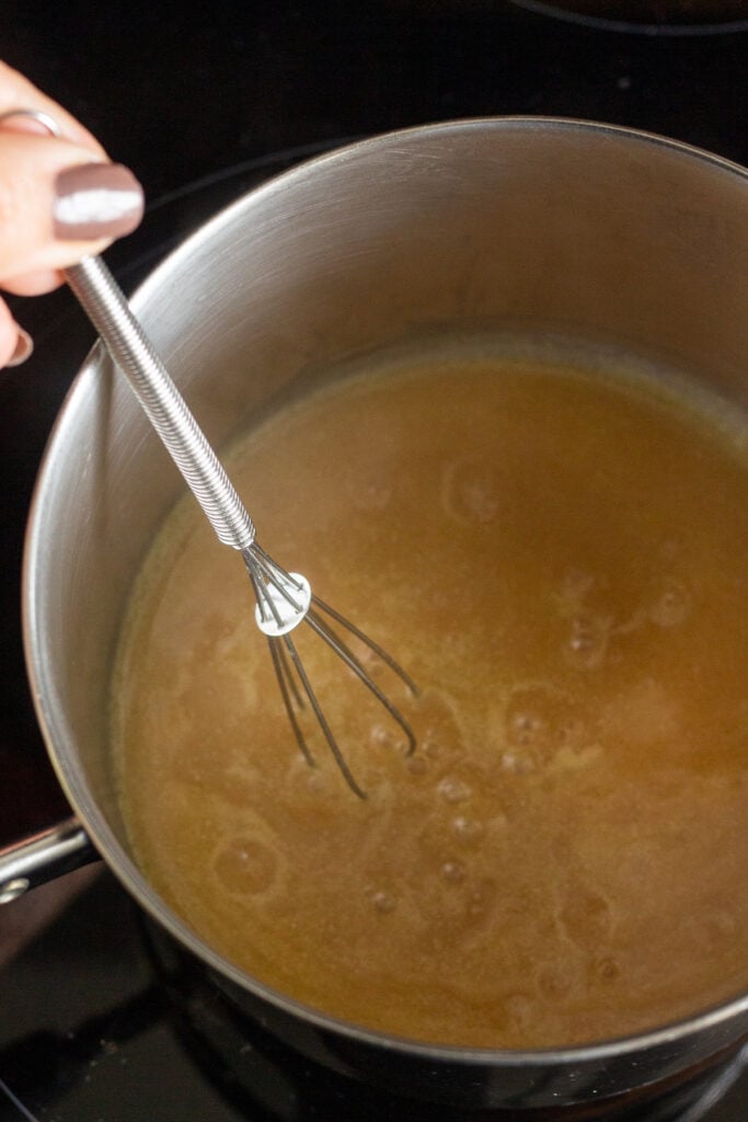 Stirring the boiling honey mustard glaze in a sauce pan on the stove with a small whisk.