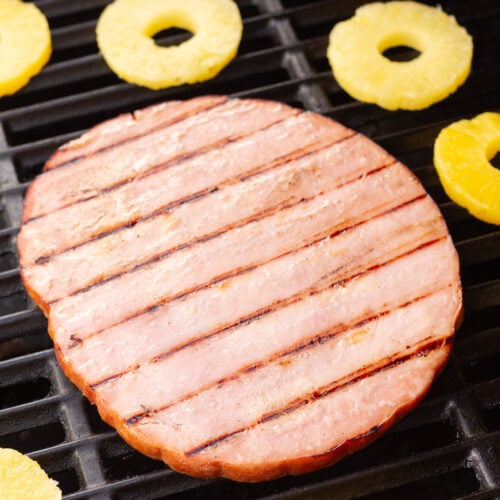 a ham steak and pineapple rings on a grill.