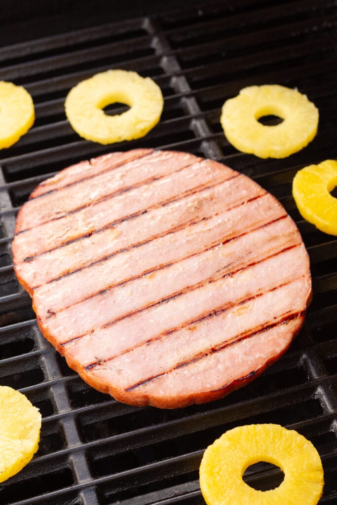 a ham steak and pineapple rings on a grill.