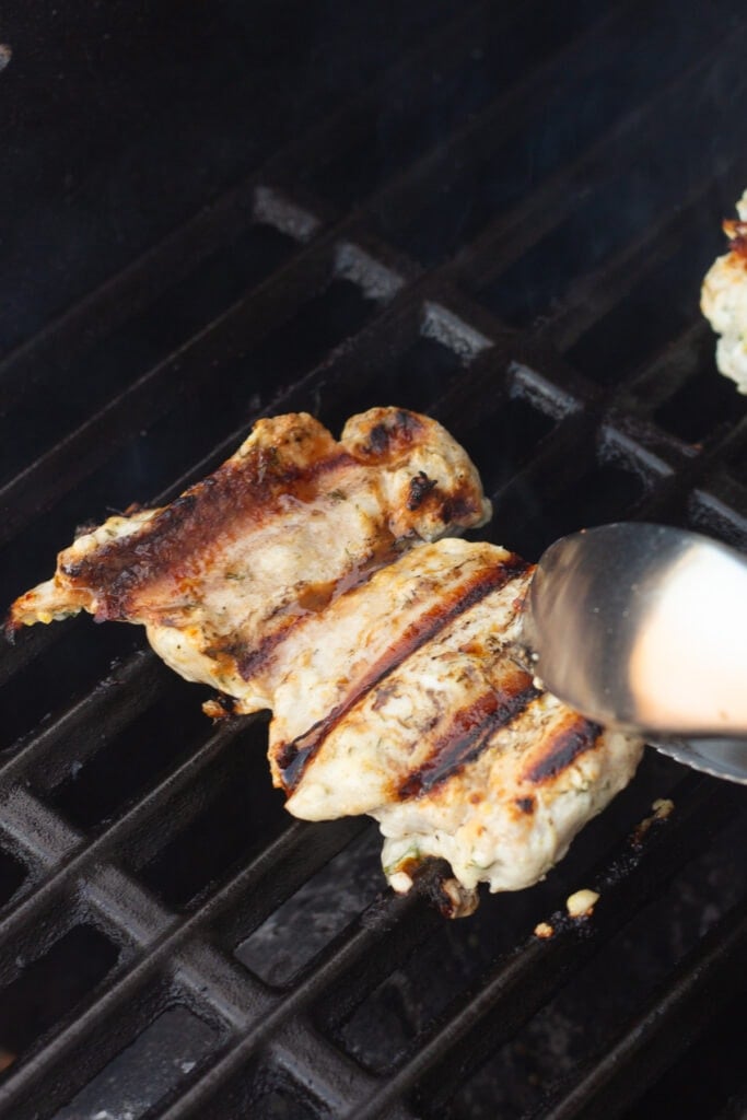 A pair of tongs flipping over Greek yogurt marinated chicken thighs on a hot grill.